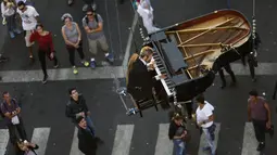 Sejumlah warga menyaksikan aksi Pianis Ricardo de Castro bermain piano di udara selama Virada Cultural di Brasil (22/6/2015). Virada Cultural merupakan acara budaya 24 jam tanpa gangguan dengan berbagai cara unik.  (AFP PHOTO/Miguel Schincariol)
