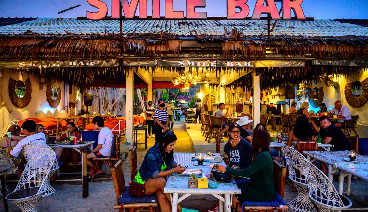 Orang-orang duduk di sebuah bar , saat para turis memanfaatkan program "Kotak Pasir Phuket" untuk pengunjung yang divaksinasi penuh terhadap virus corona Covid-19 di pulau Phuket Thailand (25/10/2021). (AFP/Mladen Antonov)