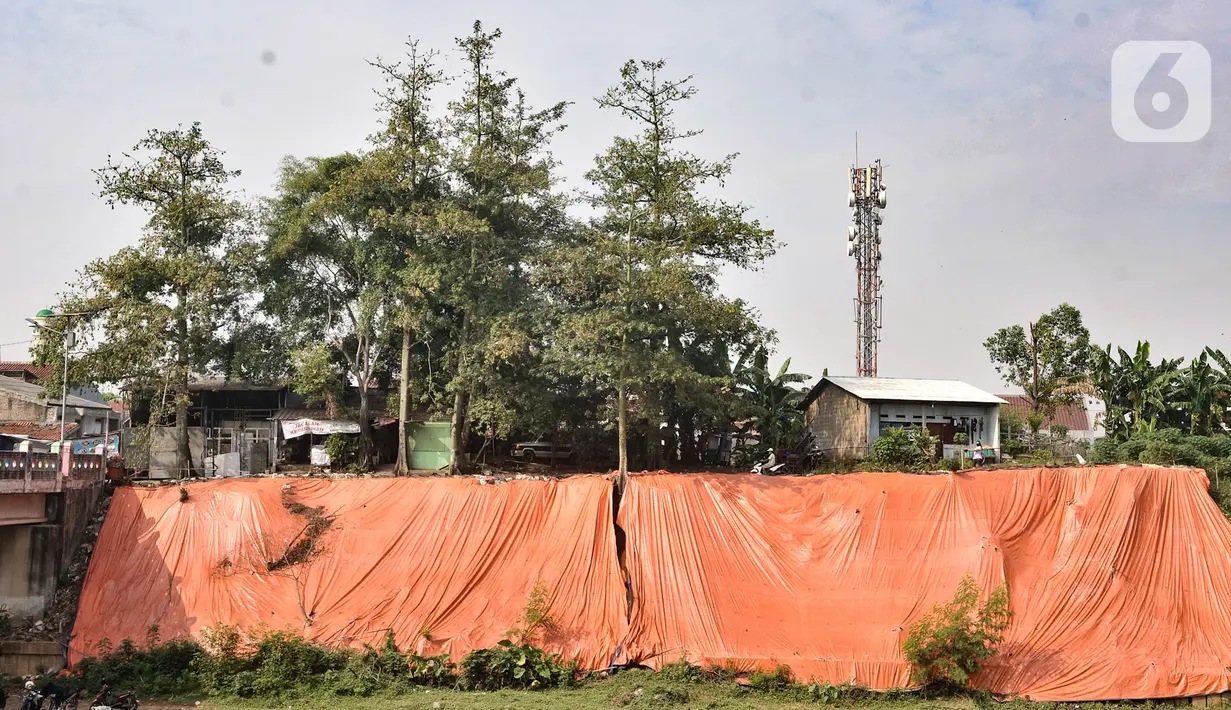 Terpal besar menutupi lokasi tanah longsor di pinggir Kanal Banjir Timur, Jakarta, Kamis (18/6/2020). Longsor yang terjadi pada awal Januari 2020 tersebut belum diperbaiki dan hanya ditutupi terpal besar guna mengantisipasi longsor susulan. (merdeka.com/Iqbal S. Nugroho)