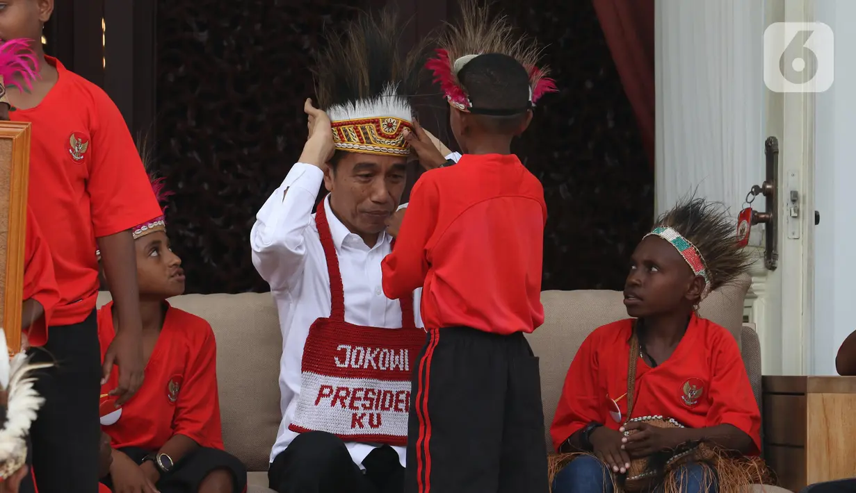 Presiden Joko Widodo atau Jokowi memasang topi rumbai saat menerima perwakilan anak-anak sekolah dasar dari Papua di Istana Merdeka, Jakarta, Jumat (11/10/2019). Jokowi mengaku sudah berjanji untuk mengundang mereka ke istana saat mengunjungi Jayapura dan Asmat. (Liputan6.com/Angga Yuniar)