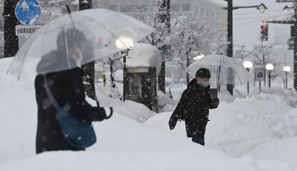 Orang-orang berjalan di atas salju yang menumpuk di depan stasiun kereta Toyama di Toyama, di pantai Laut Jepang, Senin (11/1/2021). Badai musim dingin yang dahsyat menghantam kawasan pesisir di sepanjang Laut Jepang. (Kyodo News via AP)