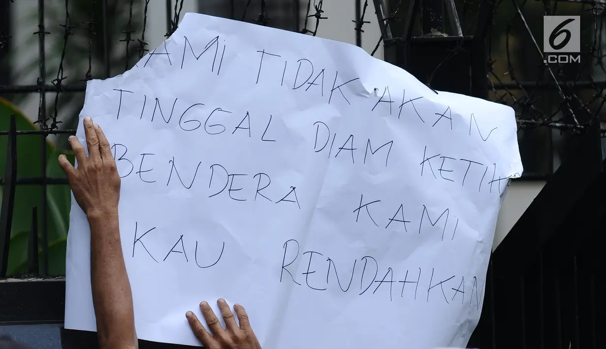 Salah satu peserta aksi menempelkan kertas pesan saat berunjuk rasa di depan Kedubes Malaysia, Jakarta, Senin (21/8). Aksi ini terkait kasus terbaliknya bendera Merah Putih pada buku panduan pelaksanaan SEA Games 2017. (Liputan6.com/Helmi Fithriansyah)