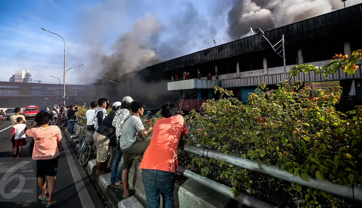 Sejumlah warga menonton petugas pemadam kebakaran yang tengah berusaha memadamkan api yang melahap pusat perbelanjaan Blok III Pasar Senen, Jakarta Pusat, Kamis (19/1). (Liputan6.com/Faizal Fanani)