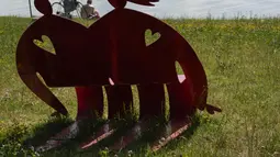 Seorang pria berjemur di samping instalasi 'Rainbow Park', karya desainer dan seniman Stefano Rossetti, di danau buatan Idroscalo, di Milan, Italia, Selasa (22/6/2021). Instalasi yang terdiri dari furnitur jalanan, patung, dan benda logam berwarna, akan dipajang hingga Juni 2022. (AP Photo/Luca Brun