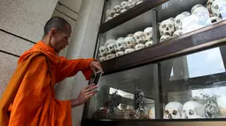 Seorang biksu saat mengabadikan Lemari kaca berisi 5.000 tengkorak manusia milik korban Khmer Merah di Phnom Penh, Kamboja, (17/4). Khmer Merah adalah sayap militer Partai Komunis Kamboja yang beraliran Maois. (REUTERS / Samrang Pring)