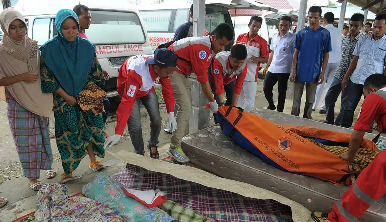 Keluarga berdiri di samping korban gempa kuat di Kabupaten Pidie Jaya, Aceh, Rabu (7/12). Seperti dirilis BMKG, gempa berkekuatan 6,4 SR mengguncang Aceh sekitar pukul 05.03 WIB. (AFP PHOTO/Chaideer Mahyuddin)