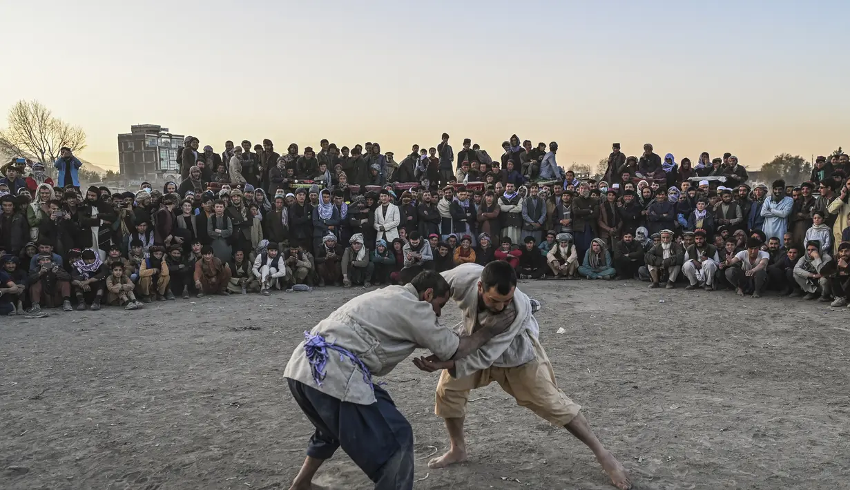 Pria Afghanistan bergulat di latar belakang selama tontonan gulat mingguan yang diadakan di arena darurat di taman Chaman-e-Hozori, di Kota Kabul (12/11/2021). (AFP/Hector Retamal)