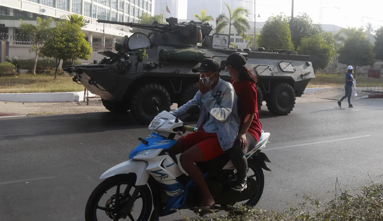 Pengendara sepeda motor melintas melewati kendaraan lapis baja yang dikerahkan di luar gedung Bank Sentral Myanmar di Yangon, Senin (15/2/2021). Pasukan militer Myanmar mulai menerjunkan kendaraan lapis baja di kota-kota besar di Myanmar dan memutus akses internet. (AP Photo)