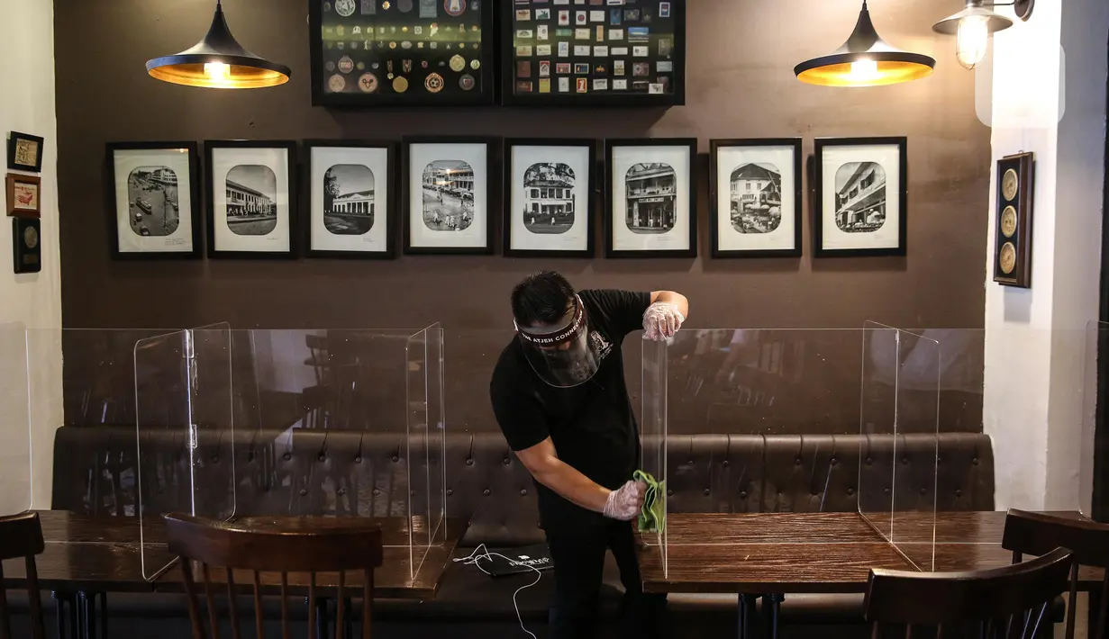 Pekerja membersihkan papan pelindung akrilik usai digunakan pengunjung di The Atjeh Connection Coffee and Resto, Jakarta, Senin (8/6/2020). Tempat ini siap menerapkan protokol kesehatan dalam menerapkan tatanan kehidupan baru atau ‘new normal’. (Liputan6.com/Faizal Fanani)