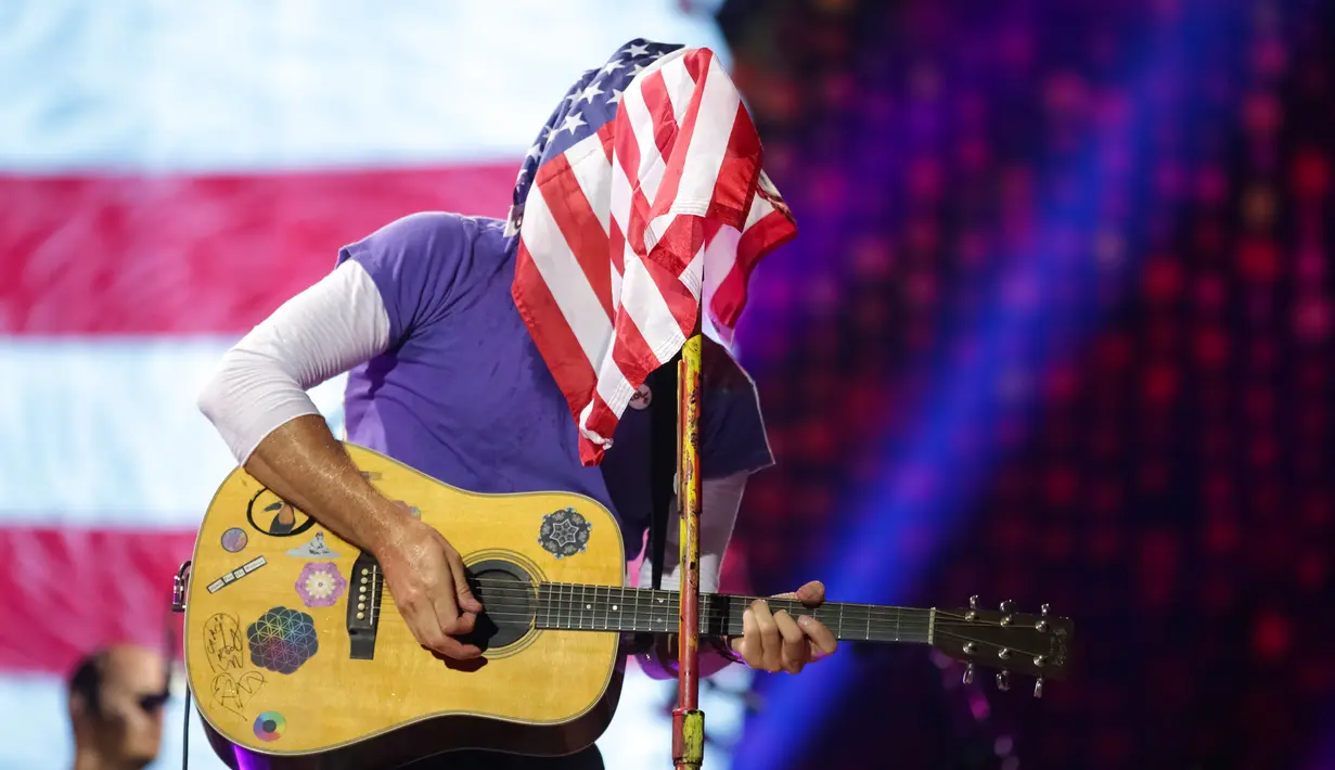 Vokalis grup band Coldplay, Chris Martin menutupi wajahnya dengan bendera Amerika Serikat sambil memainkan gitarnya saat menghibur para penonton di Lapangan FedEx di Landover, Md, AS (6/8). (Photo by Brent N. Clarke/Invision/AP)