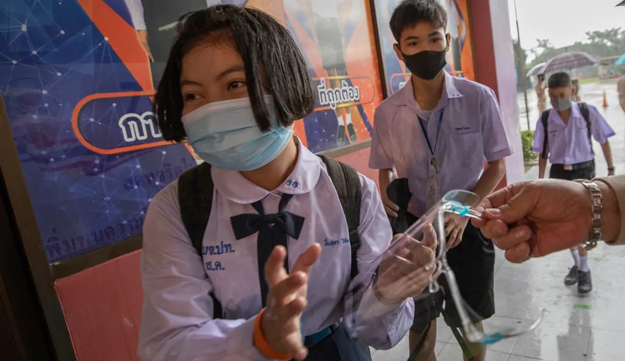 Guru memberikan pelindung wajah kepada seorang siswa di Samkhok School di Pathum Thani, Bangkok, Rabu (1/7/2020). Thailand telah memulai fase kelima relaksasi pembatasan covid-19 yang memungkinkan kembali dibukanya sekolah-sekolah setelah ditutup sejak Maret lalu. (AP/Sakchai Lalit)