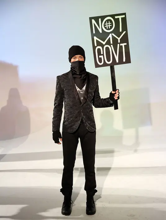Seorang model membawa poster #Not My Govt saat presentasi karya Robert James dalam NYFW di New York, (30/1). (Robin Marchant Getty Images/AFP)
