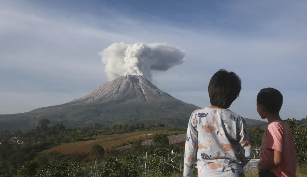Dua orang Anak menyaksikan Gunung Sinabung memuntahkan material vulkanik saat meletus di Karo, Sumatera Utara, Kamis (11/3/2021). Gunung berapi tersebut mengeluarkan longsoran awan gas membakar yang mengalir menuruni lerengnya saat terjadi letusan pada hari Kamis. (AP Photo/Binsar Bakkara)