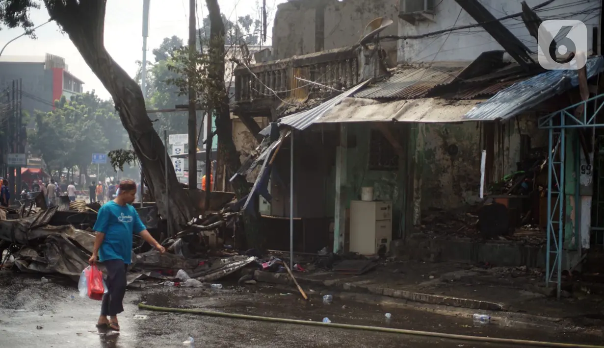 Warga berjalan melewati toko dan pemukiman yang terbakar di kawasan Manggarai, Jakarta, Selasa (7/7/2020). Hingga kini belum diketahui pengebab kebakaran. (Liputan6.com/Immanuel Antonius)