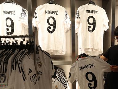 Seorang pria memegang jersey pemain sepak bola Prancis, Kylian Mbappe yang baru saja diluncurkan di toko resmi Real Madrid di stadion Santiago Bernabeu, Madrid, pada 11 Juli 2024. (Pierre-Philippe MARCOU/AFP)