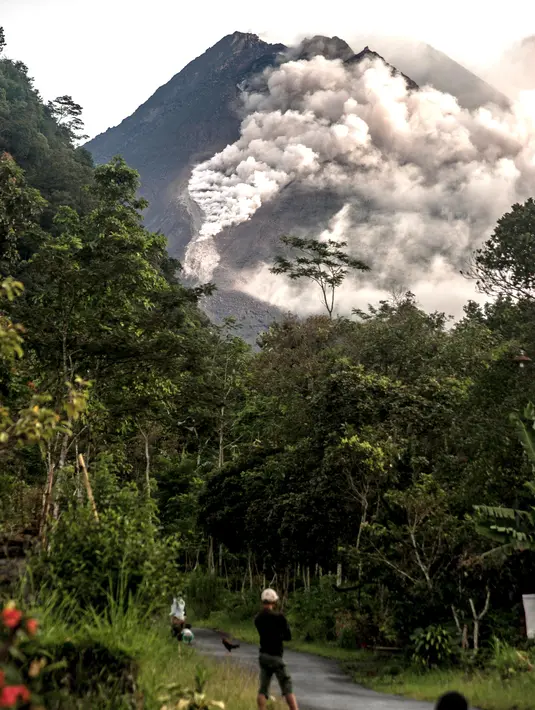 Orang-orang melihat Gunung Merapi yang memuntahkan batu dan abu di Yogyakarta (27/1/2021).  Potensi bahaya saat ini berupa guguran lava dan awan panas pada sektor selatan-barat daya meliputi sungai Boyong, Bedog, Krasak, Bebeng, dan Putih sejauh maksimal 5 kilometer.  (AFP/ Agung Supriyanto)