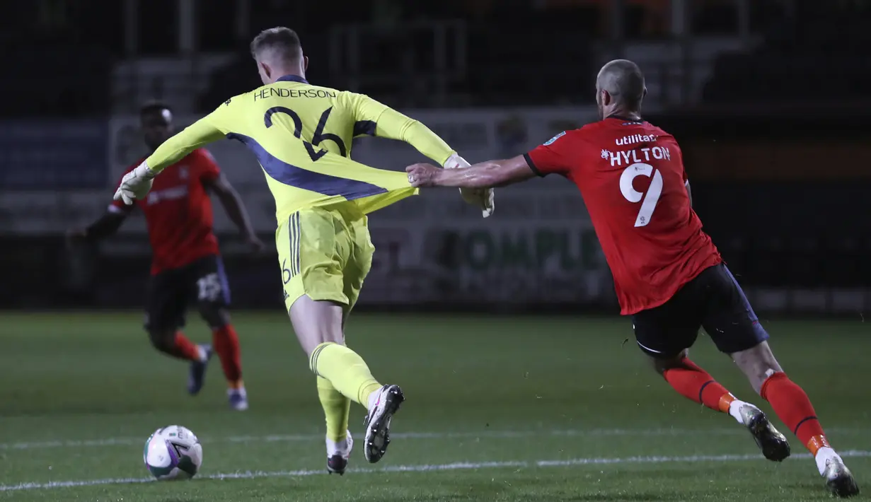 Penjaga gawang Manchester United Dean Henderson (kiri) menggiring bola meninggalkan pemain Luton Town Danny Hylton pada pertandingan babak ketiga Piala Liga Inggris di Kenilworth Road, Luton, Inggris, Selasa (22/9/2020). Manchester United mengalahkan Luton Town 3-0. (Cath Ivill/Pool via AP)