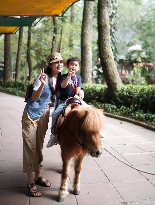 Naik kuda poni, memang menjadi salah satu spot wisata yang paling banyak disukai anak-anak. Anak-anak paling suka saat naik kuda poni mengelilingi tempat wisata. Terlihat kedua buah hatinya pun terlihat senang saat naik kuda poni. (Liputan6.com/IG/@sandradewi88)