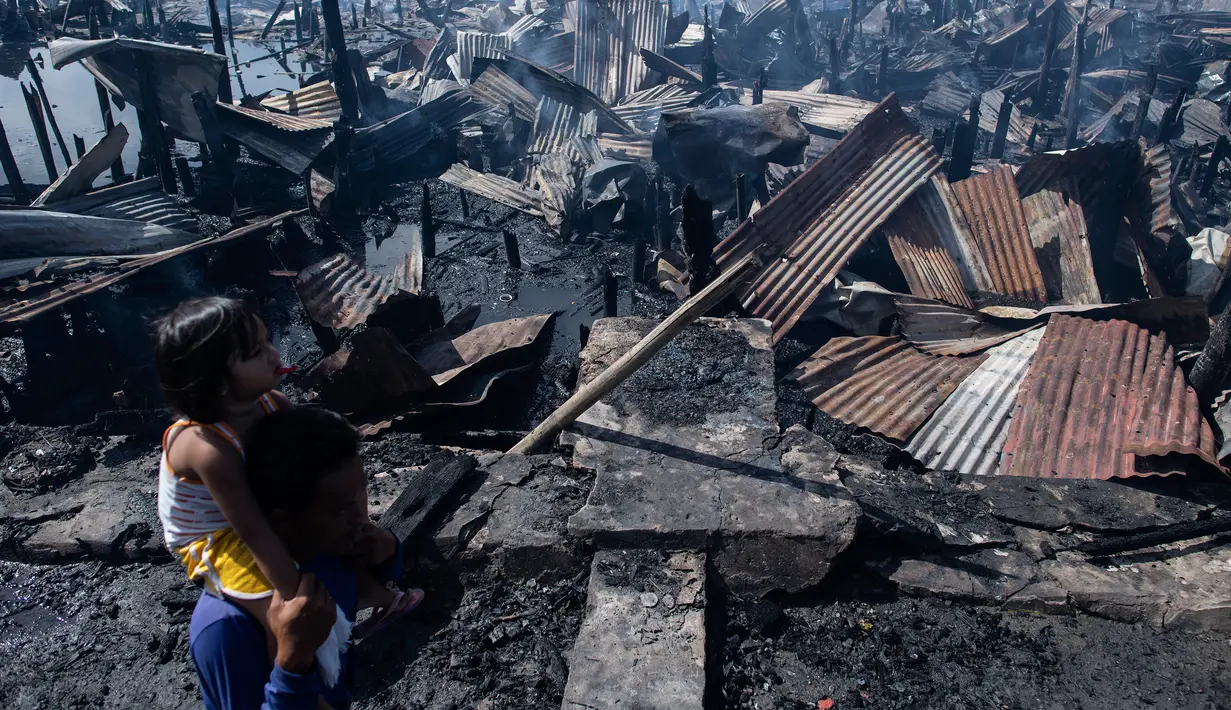 Seorang pria menggendong anaknya setelah rumah-rumah mereka hangus terbakar di sebuah daerah kumuh di Navotas, Manila (8/11). Dilaporkan sekitar 150 keluarga terkena dampak kebakaran tersebut. (AFP Photo/Noel Celis)