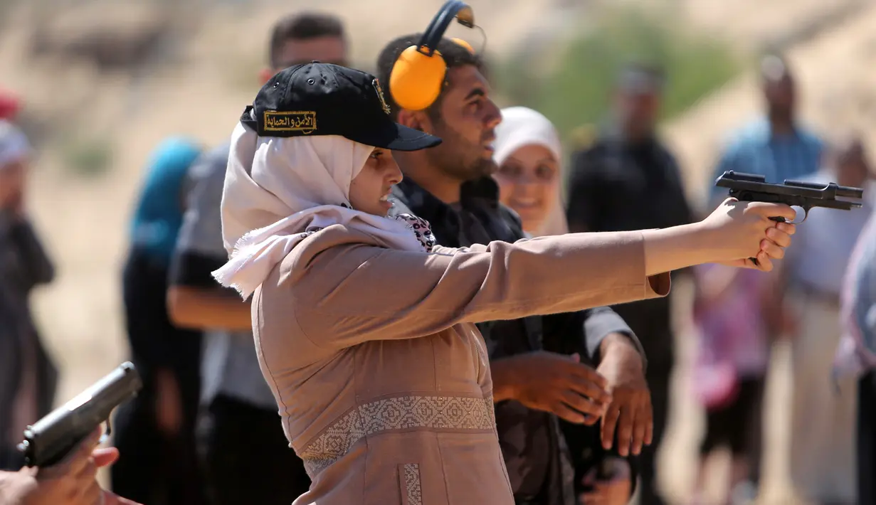 Pelatih memberikan arahan pada seorang gadis Palestina yang tengah belajar menembak saat mengikuti pelatihan dengan anggota Perlindungan dan Keamanan Hamas di Khan Younis di Jalur Gaza, Minggu (24/7). (REUTERS/ Ibraheem Abu Mustafa)