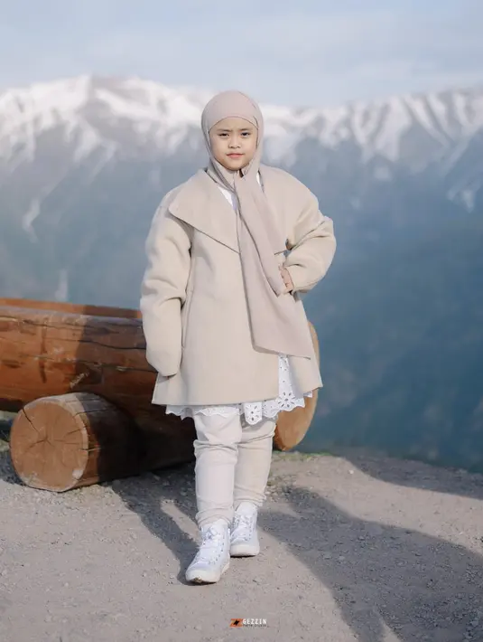 Berlatar pemandangan Indah, Maryam tampak mengenakan coat bernuansa khaki disertai hijab senada. Detail dress putih menambah pesona penampilannya menghadirkan kesan stylish yang menggemaskan. [Foto: Instagram/ Okisetianadewi]