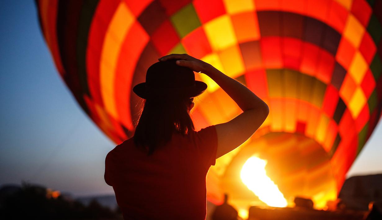 Wisatawan menyaksikan saat balon udara disiapkan untuk menikmati pemandangan Kapadokia, Turki, Selasa (7/8). Cerobong Peri Kapadokia adalah lansekap batu vulkanik berbentuk kerucut yang menjulang tinggi ke langit. (AP Photo/Emrah Gurel)