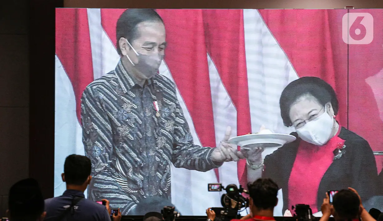Ketua Umum PDIP Megawati Soekarnoputri (kanan) mengangkat tumpeng pemberian Presiden Joko Widodo atau Jokowi (kiri) saat Rakernas II PDIP di Jakarta, Selasa (21/6/2022). Rakernas PDIP kali ini mengusung tema 'Desa Kuat, Indonesia Maju dan Berdaulat'. (Liputan6.com/Faizal Fanani)
