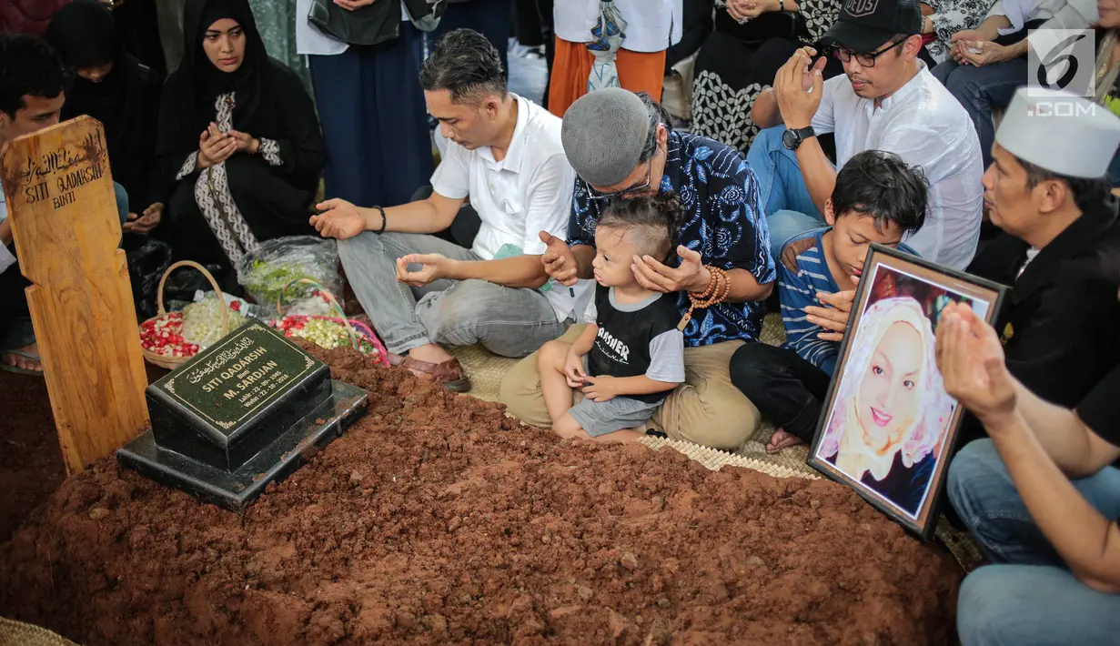 Anak aktris senior Titi Qadarsih, Indra Qadarsih memangku sang anak sambil berdoa di pusara ibunya saat dimakamkan di TPU Tanah Kusir, Jakarta, Selasa (23/10). Keluarga Titi tampak tabah menerima kepergian ibu dan nenek mereka. (Liputan6.com/FaizalFanani)