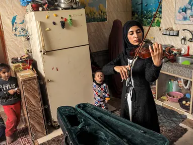 Musisi Palestina Jawaher al-Aqraa memainkan biola sambil berdiri di dapur rumahnya di Deir al-Balah, Jalur Gaza Tengah, 24 Oktober 2023. (Eyad BABA/AFP)