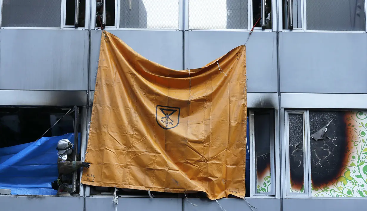 Petugas pemadam kebakaran menggunakan lembaran plastik untuk menutupi jendela sebuah gedung, tempat kebakaran terjadi di Osaka (17/12/2021). Kebakaran terjadi di lantai empat atau lima sebuah gedung berlantai delapan di kawasan perbelanjaan dan hiburan di kota Osaka. (AFP/STR/Jiji Pers)