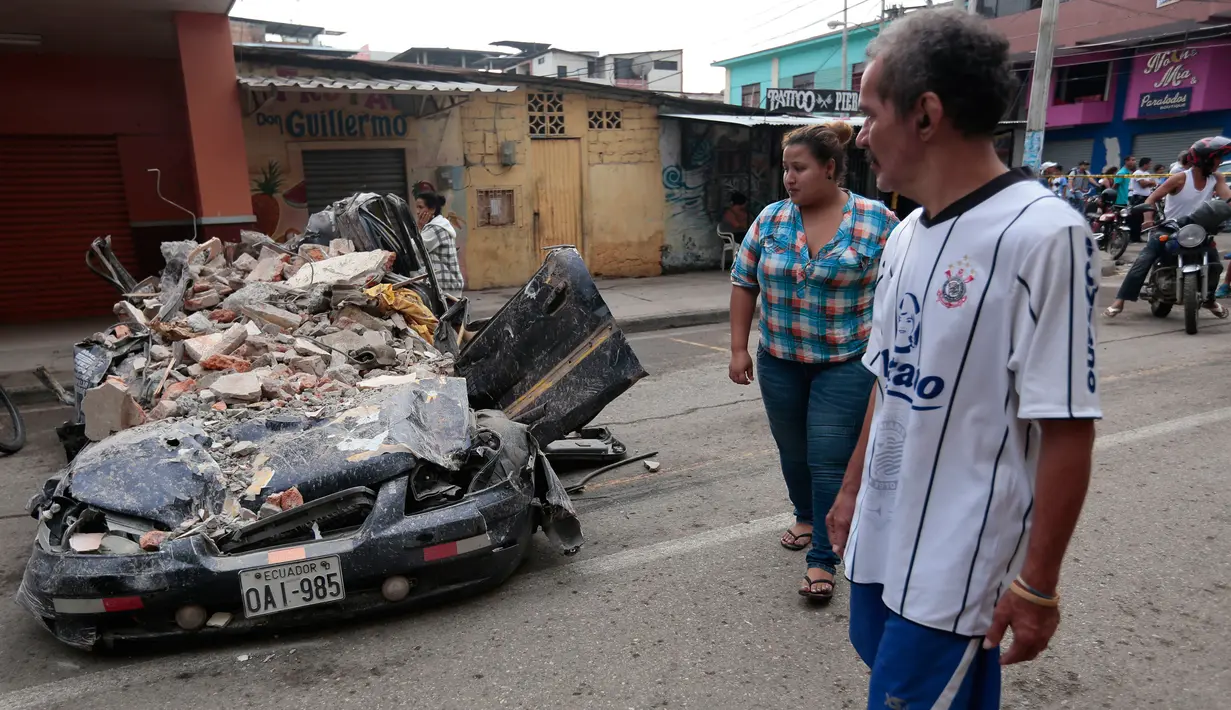 Warga mengamati sebuah mobil yang tertimpa reruntuhan bangunan setelah gempa 7,8 SR mengguncang Portoviejo, Ekuador, Minggu (17/4). Hingga hari ini (18/4/2016), sudah 246 orang meninggal dan 2.527 lainnya terluka.  (Juan Cevallos/AFP)