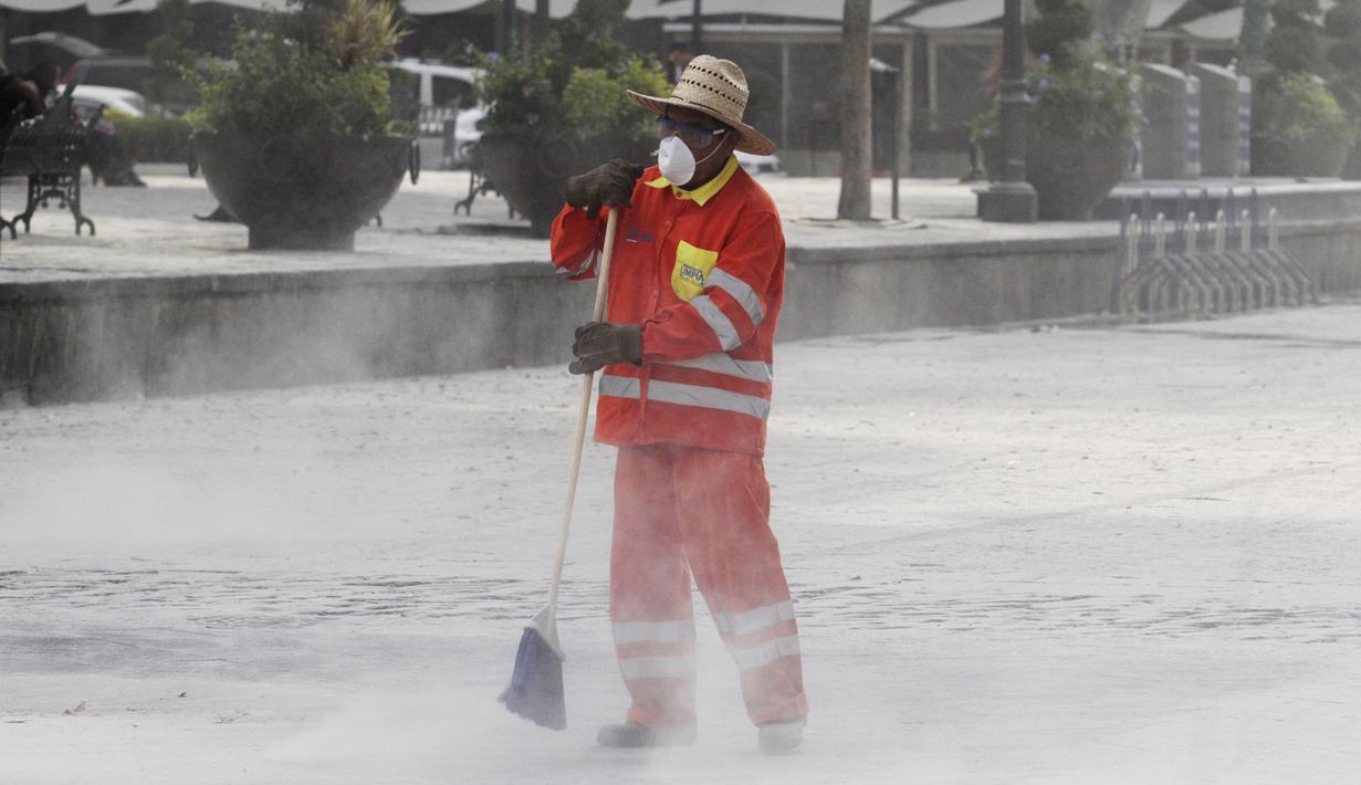 Petugas memakai masker membersihkan jalan yang tertutup abu setelah letusan awal gunung berapi Popocatepetl di Puebla, Meksiko, (18/4). Pemerintah Meksiko mengatakan gunung Popocatepetl menyemburkan abu vulkanis setinggi 3 km. (REUTERS/Imelda Medina)