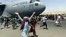 Ratusan orang berusaha menaiki pesawat angkut C-17 Angkatan Udara AS di landasan bandara internasional, di Kabul, Afghanistan (16/8/2021).  Di tengah kekacauan pasca direbutnya Ibukota Kabul oleh pasukan Taliban, dua warga jatuh dari pesawat militer Amerika Serikat. (Verified UGC via AP)