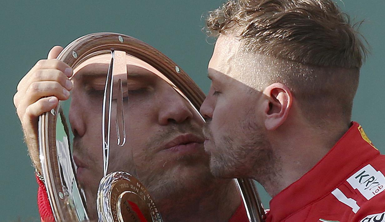 Pebalap Ferrari, Sebastian Vettel mencium trofi usai memenangi balapan F1 GP Australia di Sirkuit Albert Park, Melbourne, Minggu (25/3/2018). Vettel memenangi balapan dengan selisih 5,036 detik dari Hamilton. (AP/Rick Rycroft)
