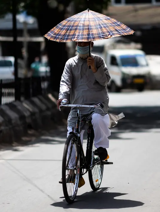 Seorang pria menaungi dirinya dengan payung saat mengendarai sepeda di tengah meningkatnya suhu di New Delhi, India, Rabu (27/5/2020). New Delhi mencatat hari terpanas di bulan Mei dalam 18 tahun terakhir dengan suhu mencapai 47,6 derajat Celcius. (Jewel SAMAD/AFP)
