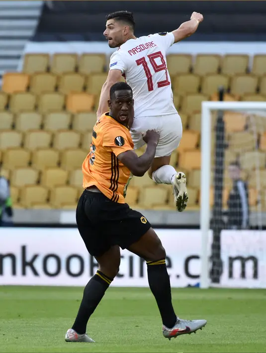Pemain Olympiakos, Giorgos Masouras melompat di atas bek Wolverhampton Wanderers, Willy Boly pada leg kedua babak 16 besar Liga Europa di Molineux Stadium, Kamis (6/8/2020). Wolverhampton menumbangkan Olympiakos dengan skor 1-0. (AP Photo/Rui Vieira)
