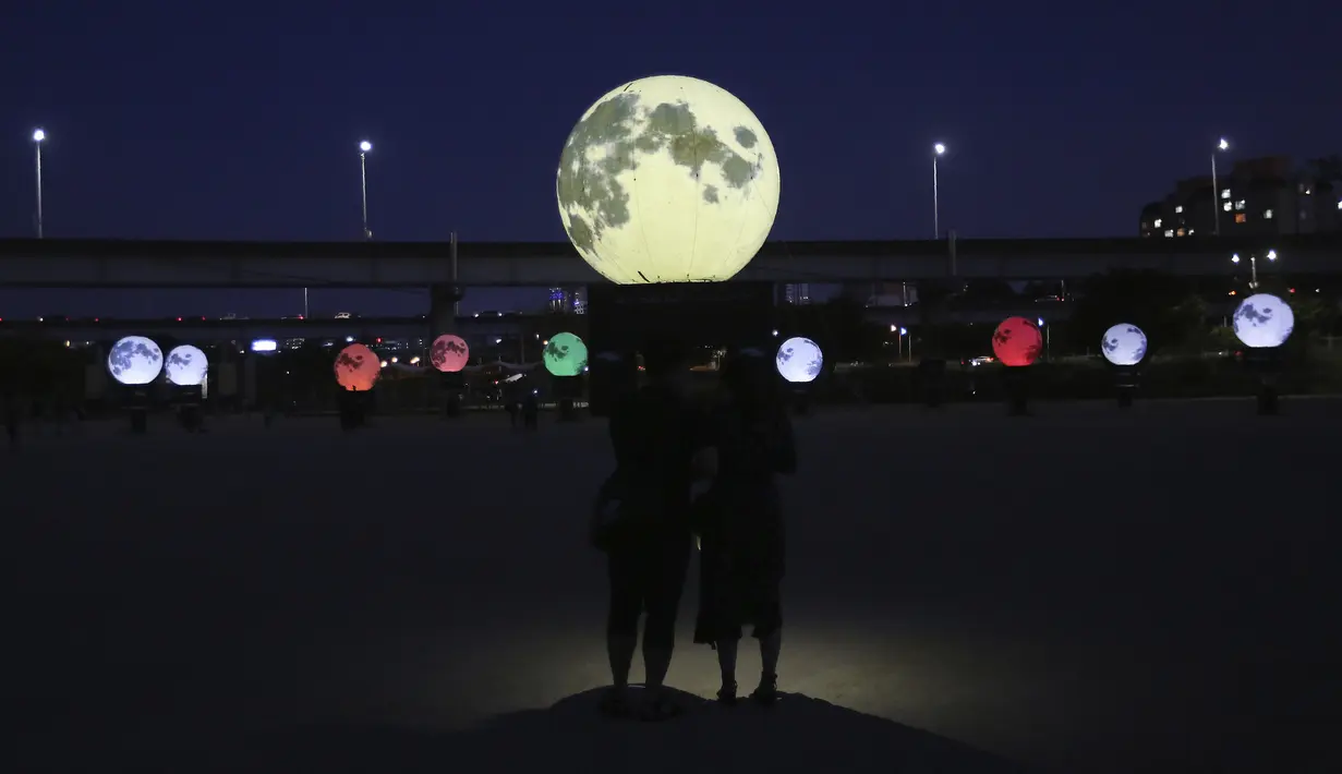 Pasangan memandangi instalasi bulan purnama yang bersinar di sebuah taman di Seoul, Korea Selatan, Jumat (18/9/2020). Pejabat setempat memasang bulan purnama buatan untuk meningkatkan semangat saat wabah COVID-19 sekaligus menyambut Chuseok, Thanksgiving versi Korea. (AP Photo/Ahn Young-joon)