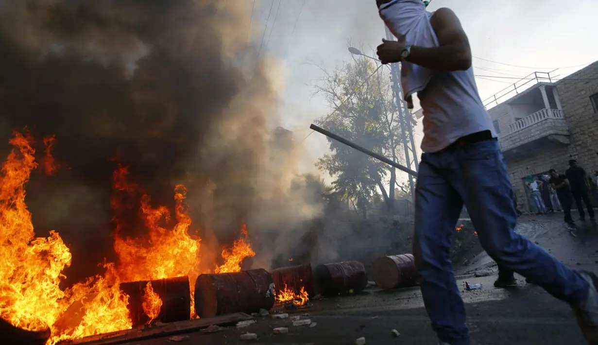 Salah satu pengunjuk rasa mencoba melewati kobaran api yang menutup jalan utama antara Bethlehem dan Hebron pasca terjadi bentrokan dengan militer Israel di Beit Ommar, utara kota Hebron, (25/7/2014). (REUTERS/Mussa Qawasma)