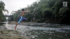 Seorang anak melompat ke Sungai Ciliwung, Depok, Jawa Barat, Kamis (4/7/2019). Menurunnya debit air Sungai Ciliwung akibat musim kemarau dimanfaatkan warga setempat sebagai tempat wisata gratis untuk mengajak anak berenang. (merdeka.com/Iqbal Nugroho)