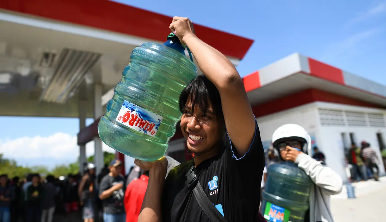 Korban gempa dan tsunami membawa bahan bakar minyak (BBM) di SPBU Kota Palu, Sulawesi Tengah, Senin (1/10). Sebelumnya, warga nekat menjarah BBM yang tersisa di dalam mobil tangki milik Pertamina pada Sabtu, 29 September 2018. (Jewel Samad/AFP)