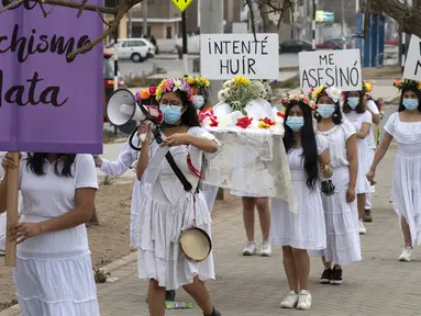 Rombongan teater Vichama melakukan prosesi kamar mayat berjudul "Kami Ingin Diri Sendiri Hidup!" sambil membawa tubuh tiruan dan menampilkan tanda-tanda kiasan pada malam Hari Anti Kekerasan Terhadap Perempuan di Villa El Salvador, Lima, Peru, 24 November 2021. (Cris BOURONCLE/AFP)