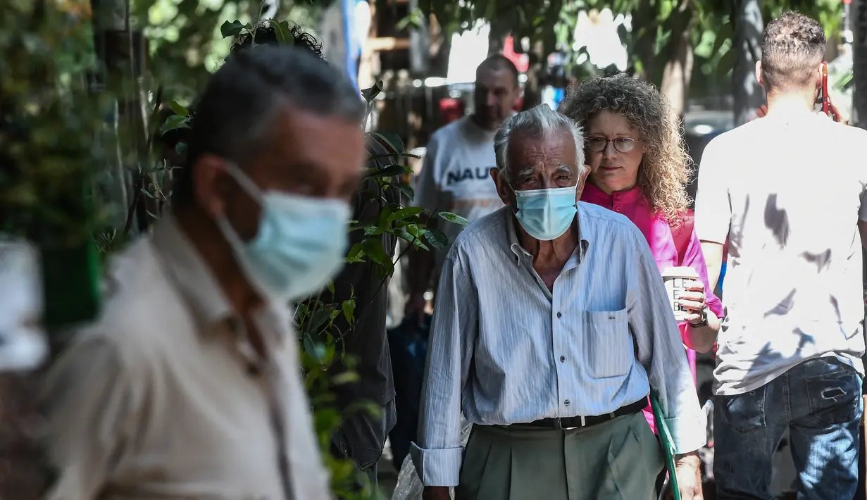Pejalan kaki berjalan di jalan mengenakan masker di pusat Thessaloniki, Yunani utara (18/5/2022). Mulai 16 Mei, masker wajah tidak lagi diperlukan di banyak penerbangan di Uni Eropa, tetapi Yunani telah mempertahankan aturan maskernya. (AFP/Sakis Mitrolidis)