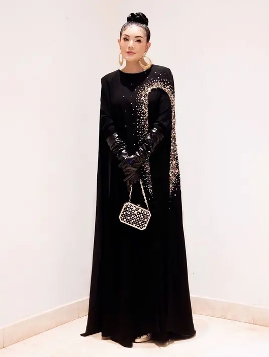 Nindy Ayunda kenakan cape dress berwarna hitam dengan latex gloves. Outfit ini bisa kamu kenakan untuk halal bihalal yang formal dan glamor. [@nindyayunda]