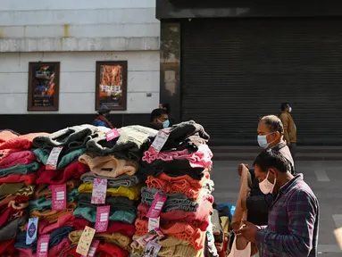 Orang-orang membeli pakaian dari kios-kios yang didirikan di luar gedung bioskop di New Delhi (29/12/2021). Pemerintah Delhi memberlakukan pembatasan fasilitas seperti gedung bioskop, multipleks, dan gym, dan lainya untuk mengekang lonjakan virus corona Covid-19. (AFP Photo/Sajjad Hussain)