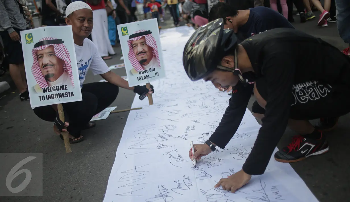 Seorang pria memegang poster sambil mengamati pengunjung Car Free Day (CFD) menandatangani spanduk berisi petisi mendukung kedatangan Raja Arab Saudi, Salman bin Abdulazis Al Saud, di Bundaran HI, Jakarta, Minggu (26/2). (Liputan6.com/Faizal Fanani)