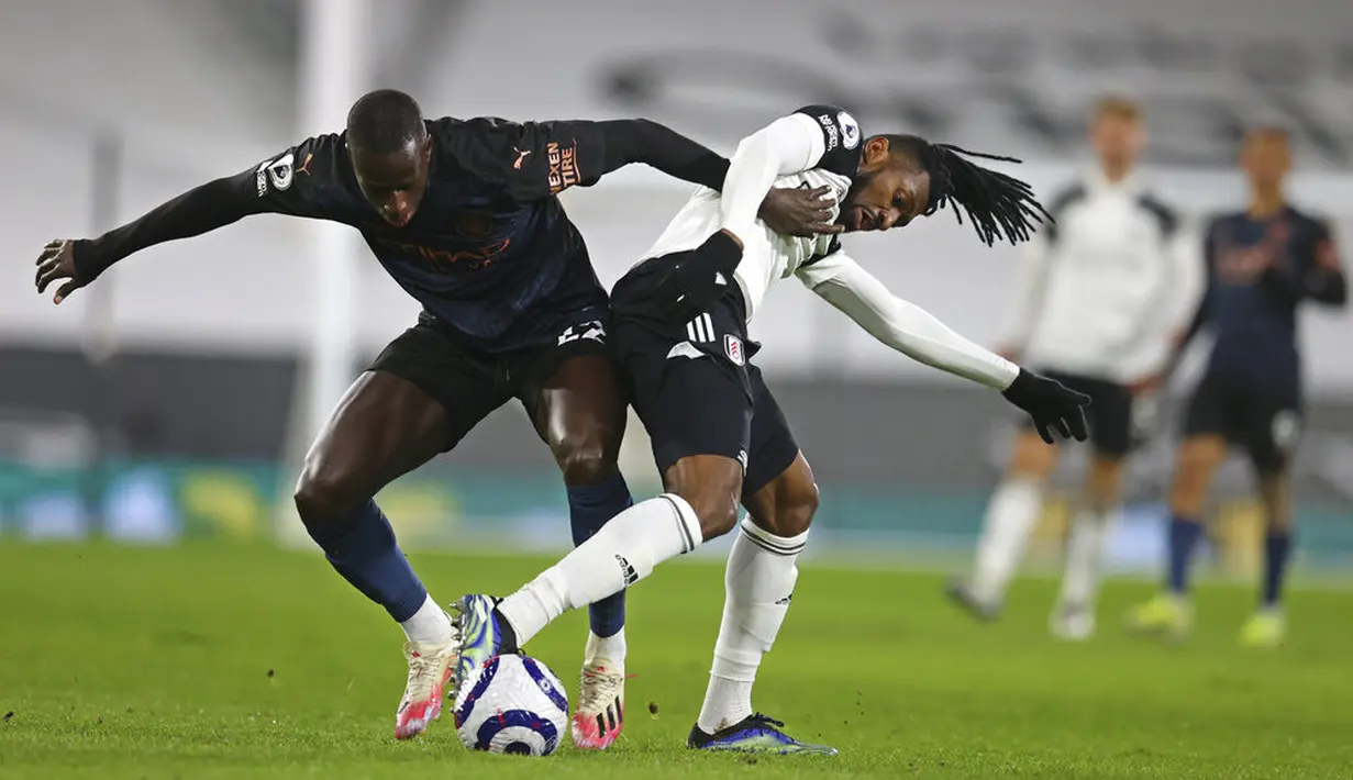 Bek Manchester City, Benjamin Mendy, berebut bola dengan pemain Fulham, Andre-Frank Zambo Anguissa, pada laga Liga Inggris di Stadion Craven Cottage, Sabtu (14/3/2021). City menang dengan skor 3-0. (Catherine Ivill/Pool via AP)