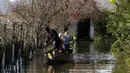 Seorang pria dengan anak-anak menaiki sampan melewati banjir setelah hujan lebat di Desa Obot, sekitar 100 kilometer (60 mil) barat laut Tirana, Albania, Senin (11/1/2021). Hujan deras dan salju selama beberapa hari terakhir telah membanjiri banyak kawasan di Albania. (AP Photo/Hektor Pustina)