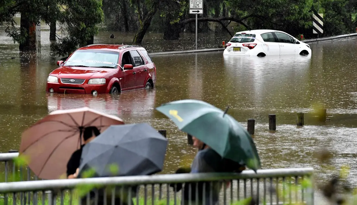 Warga melihat mobil yang terendam banjir di pinggiran barat daya Sydney, Australia, Selasa (8/3/2022). Ribuan warga Sydney diminta untuk mengungsi dari daerah dataran rendah karena hujan lebat dan banjir bandang. (Muhammad FAROOQ/AFP)