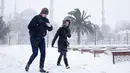 Sepasang warga berjalan menembus timbunan salju di tengah badai di kawasan Sultanahmet, distrik wisata bersejarah di Istanbul, Sabtu (7/1). Badai salju dahsyat melumpuhkan Kota Istanbul. (Mert Akyol/Depo Photos via AP)
