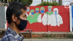 Warga melintas di depan mural bertema covid-19 di Bukit Duri, Jakarta, Minggu (30/8/2020). Mural yang dibuat petugas PPSU bertujuan untuk mengingatkan masyarakat akan bahaya covid-19, sehubungan dengan masih tingginya jumlah kasus positif covid-19 di Jakarta. (Liputan6.com/Immanuel Antonius)